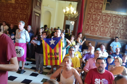 Imagen de asistentes al pleno con banderas en qué se puede leer 'sí' y 'queremos votar'.