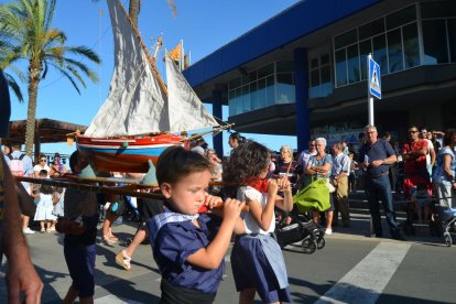 Uns nens vestits de pescadors porten un vaixell a espatlles.