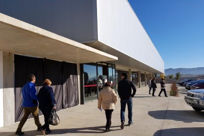 Plan|Plano general de la entrada en el pabellón de Roquetes este 21-D por la mañana con los votantes pasando por delante del mural de Ignasi Blanch tapado con plásticos negros.