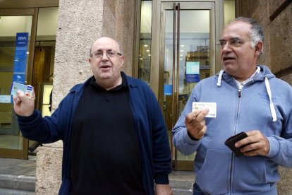 Ramon Pàmies y Joan Moncusí mostrando sus tarjetas de crédito después de retirar 150 euros en un cajero del BBVA de la plaza Prim de Reus.