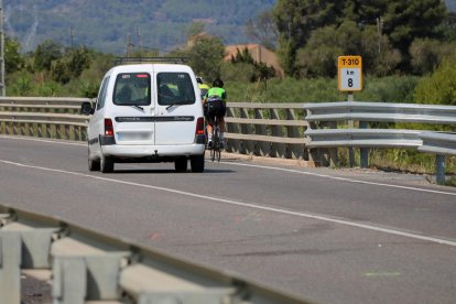 Pla general del punt quilomètric 8 de la T-310 entre Riudoms i Montbrió, amb un grup de ciclistes circulant mentre un cotxe els intenta avançar hores després d'un accident mortal amb dos ciclistes en el mateix punt.