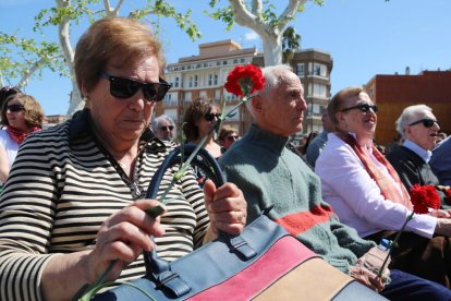 Primer pla de diversos supervivents als bombardeigs durant l'acte d'homenatge amb un clavell a la mà preparat per llençar al riu.