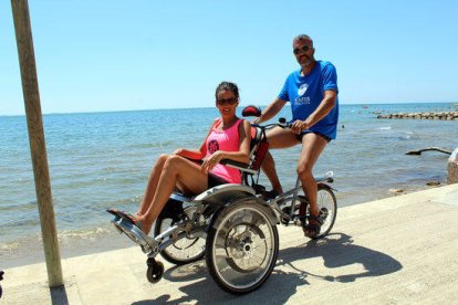 Una parella passeja prop de la platja amb una cadira-bicicleta adaptada OPair.