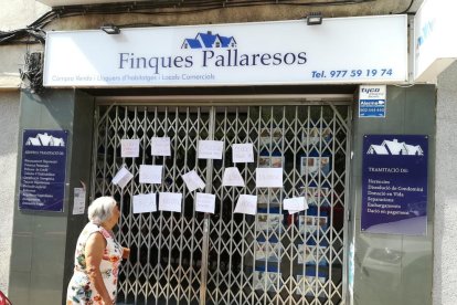 Una veïna llegeix el contingut dels cartells col·locats a la tanca de l'antiga oficina de les finques.