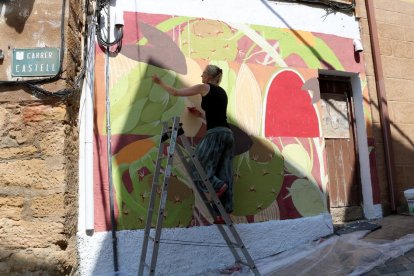 Una de las artistas participantes en la edición 2018 del concurso Riu d'Art de Riba-roja d'Ebre conversando delante de una de las puertas que ha pintado con dibujos inspirado en historias locales.