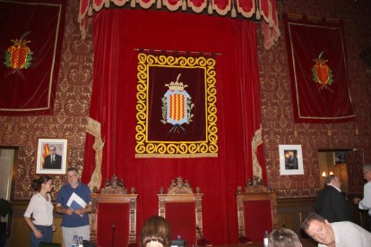 Pla general del saló de plens, amb l'escut municipal presidint-lo, la foto de Quim Torra a l'esquerra i la de Felip VI a la dreta de la imatge.