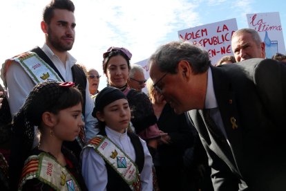 El president de la Generalitat, Quim Torra, rebut per dues nenes en la seva arribada al Centre Fluvial del Delta i amb pancartes al fons de protesta.