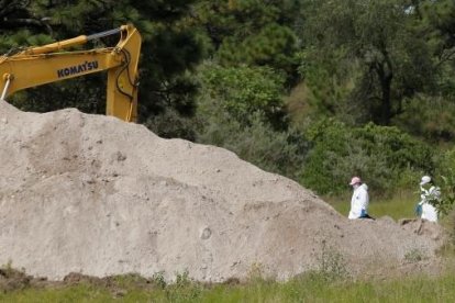 Peritos forenses trabajando en la fosa clandestina al lado de maquinaria pesada.