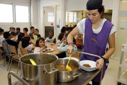 Una monitora sirviendo comida al plato en el comedor escolar.