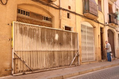 Una gran porta de ferro tapiant un immoble vell que es pretenia ocupar al barri del Carme de Reus, i al fons, un veí del barri, observant.