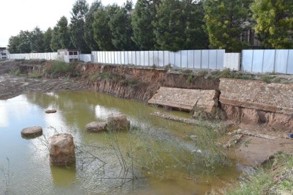 El mur ha caigut pels efectes de la pluja, que manté el solar ple d'aigua.