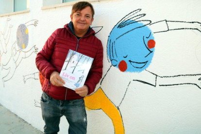 L'il·lustrador Ignasi Blanch amb un exemplar del llibre-disc 'LIV ON' al costat dels seus dibuixos al pati de l'escola de Xerta.