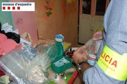 Un agent dels Mossos d'Esquadra inspeccionant les drogues i altres efectes intervinguts en un pis de Roquetes.