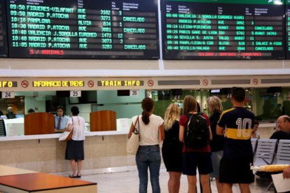 Imagen de usuarios de Renfe haciendo cola en la taquilla de información bajo el cartel de salidas y llegadas a la estación de Sants.