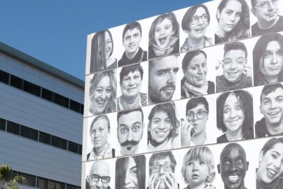 Un grupo de jóvenes pasa por delante de la fachada de Lo Pati donde se encuentran enganchados los retratos de #mosmirem.