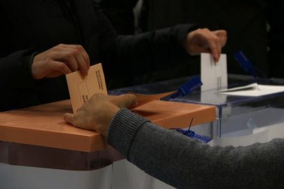 Plano detalle de una mano depositando las papeletas de las elecciones en el Congreso de los diputados y al Senado en una urna.