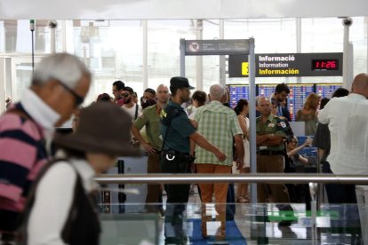 Pasajeros pasando el control de seguridad delante de un agente de la Guardia Civil y dos vigilantes a la T1 del aeropuerto del Prat.