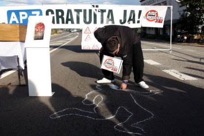 Un jove pinta una silueta a l'asfalt de l'N-340 a les Cases d'Alcanar mentre porta un cartell que reclama la gratuïtat de l'AP-7.