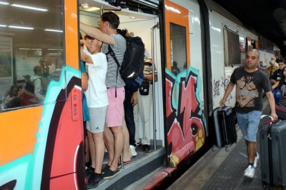 Pla general d'una porta d'un tren de Rodalies aturat a l'estació de Sants, amb els vagons plens de gent.