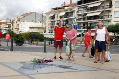 Plano abierto de varias personas paradas delante del Memorial per la Pau de Cambrils, con un ramo de flores.