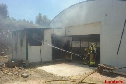 Dos bomberos remojando el cobertizo que ha quemado.