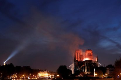 La Catedral de Notre-Dame de París en llamas durante la noche, con bomberos remojando el edificio para intentar salvar las torres.