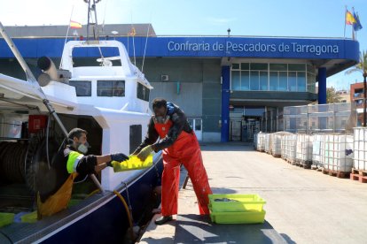 Dos pescadores empezando a descargar cajas de pescado de una barca de arrastre.