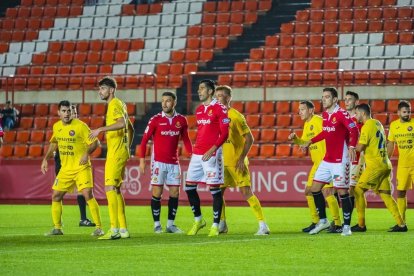 David Goldar, Gerard Oliva i Juan Rodríguez envoltats de jugadors de l'Olot durant el duel de Copa del Rei d'aquesta temporada.