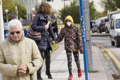 Una chica con máscara andando con su madre por la calle.