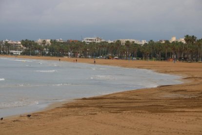 La platja de Llevant de Salou amb només algunes persones passejant vora el mar.