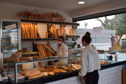 Interior de una tienda de Igualada con una dependienta con mascarilla poniendo una barra de pan dentro de una bolsa.