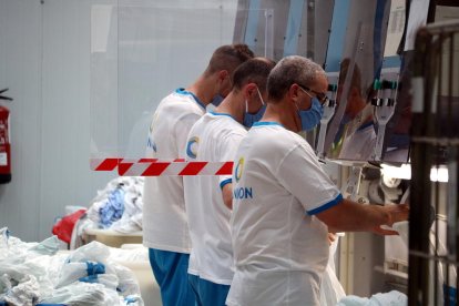 Tres trabajadores de la lavandería Ilunion de Tortosa poniendo sábanas en la máquina que las dobla.