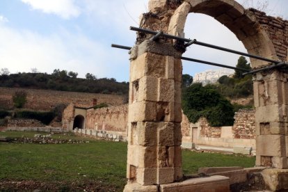 Un arc del claustre major de la Cartoixa d'Escaladei en primer terme, amb el pati al darrer i, al fons, la silueta del Montsant.