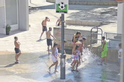 Un grup es refresca amb l'aigua a pressió, en una plaça del barri.