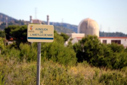 Un cartell amb el nom d'un carrer a l'Ametlla de Mar (Baix Ebre) amb la central nuclear de Vandellòs (Baix Camp), desenfocada, al fons.