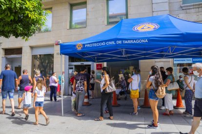 Una vintena de persones esperant per fer gestions a l'OMAC i protegint-se del sol ahir a mig matí.