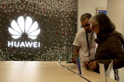 Un dependent mostra a una senyora un dispositiu mòbil a la botiga de Huawei de plaça Catalunya