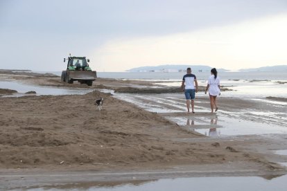 Dues persones i un gos caminant a prop d'una màquina treballant a la barra del Trabucador.