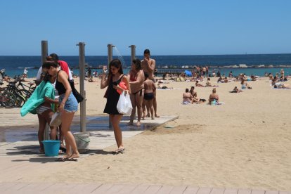 Diverses persones a les dutxes, a la platja de Sant Miquel, a Barcelona