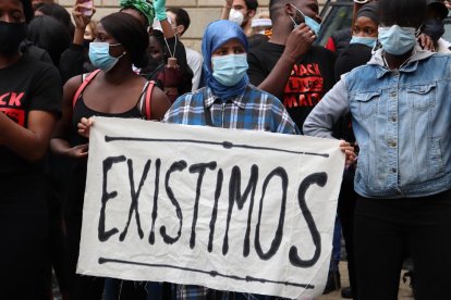 Una manifestante sostiene una pancarta que dice 'Existimos' en la concentración contra el racismo en la plaza Sant Jaume de Barcelona.