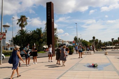 Turistes al passeig marítim de Cambrils, mirant encuriosits les flors i ciris al terra.