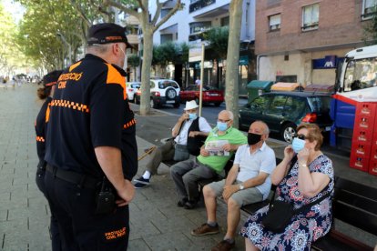 Dos voluntarios de Protección Civil controlando el uso de mascarilla entre varios vecinos de Reus sentados en un banco en el paseo Sunyer.