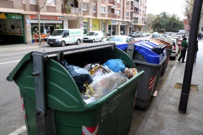 Plano abierto de una isla de contenedores de la calle de Cambrils de Reus, con un contenedor de rechazo lleno de basura en primer término.