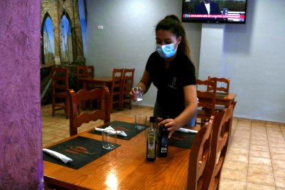 Plano medio de la camarera del bar restaurante Farcit de Tortosa poniendo vinagreras en las mesas para recibir los clientes para comer.