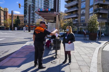 Un voluntario de Protección Civil entregando una mascarilla a una usuaria de la EMT en la parada de la plaza Imperial Tàrraco.