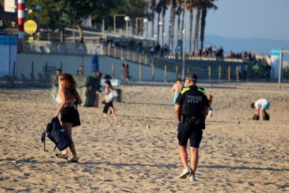 Una chica abandona la playa de la Nova Icària, al lado de un agente policial, poco antes de que cerrara al público para esta Noche de Sant Joan.