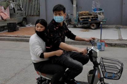 Dues persones que circulen amb moto per un mercat de Pequín, la Xina, porten màscara.