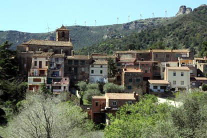 Pla general d'una panoràmica del poble de l'Argentera, al Baix Camp, amb l'església sobresortint d'entre els edificis i, al fons al darrere, molins d'energia eòlica damunt la muntanya