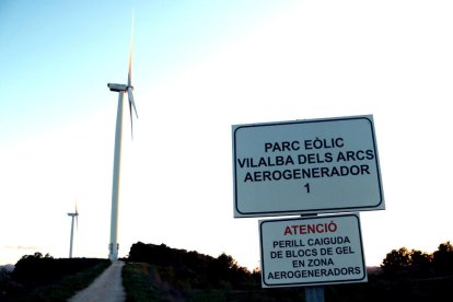 Un cartel señalizando un parque eólico en Vilalba dels Arcs, en la Terra Alta, con dos aerogeneradores en el fondo.