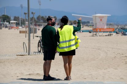 Dos informadores municipales, de espaldas, en la playa del Bogatell.